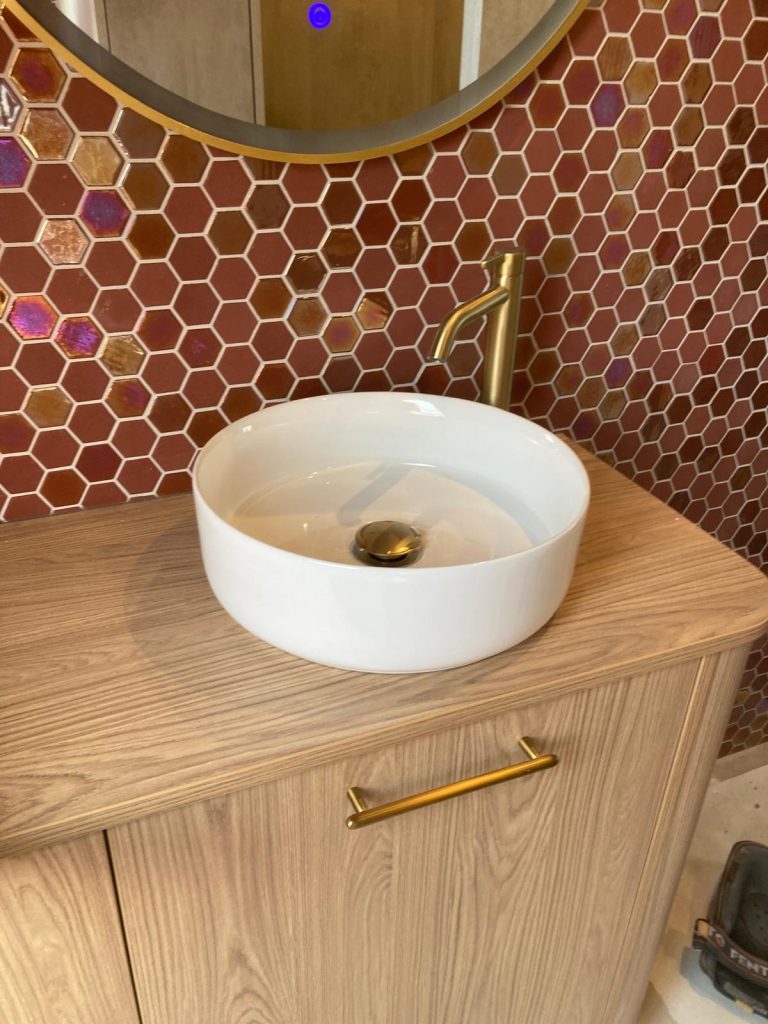 Waskom op houten badmeubel met gouden kraan en rode mozaïektegels